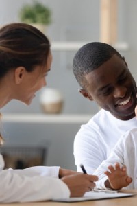 Cheerful young female pediatrician and african american smiling father listening to mixed race little patient, telling doctor about well-being. Happy multiracial family visiting clinic for check up.
